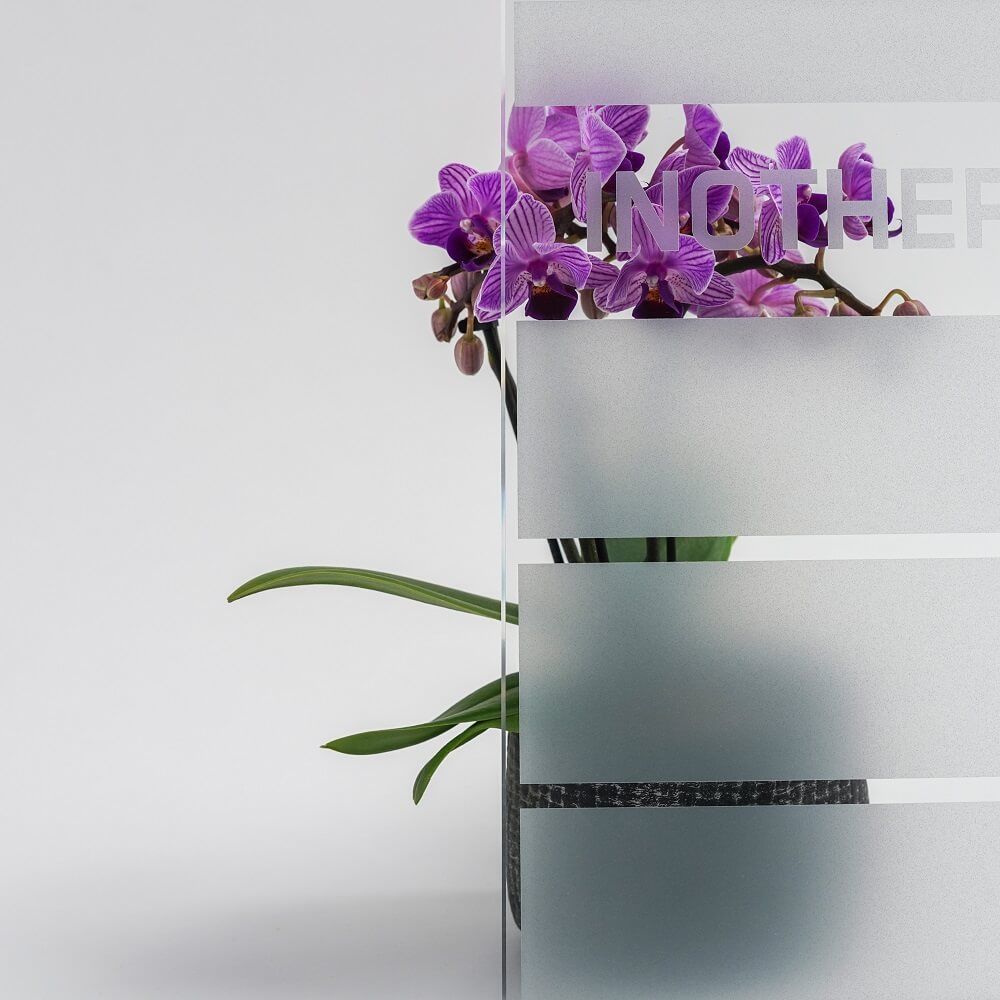 Orchideenblüten in einer Vase hinter mattiertem Glas mit horizontalen Streifen und eingraviertem Text.
