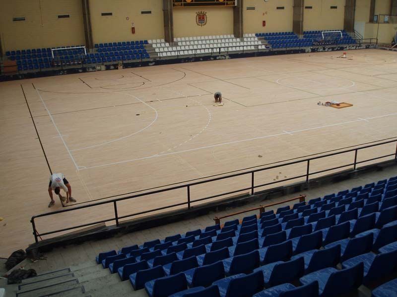 Un hombre está trabajando en una cancha de baloncesto en un estadio con asientos azules.
