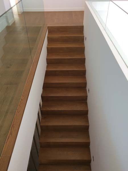 Las escaleras son de madera y tienen barandilla de cristal.
