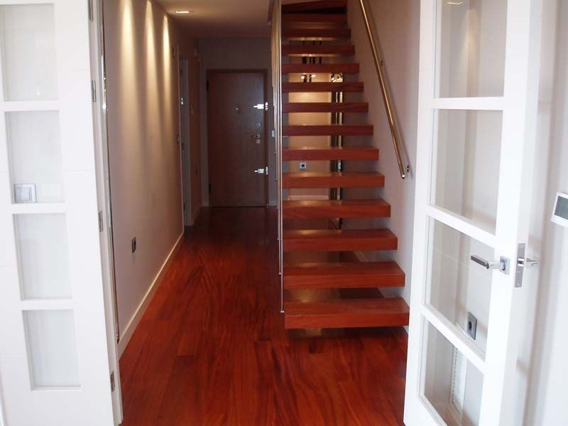 Un pasillo con escalera de madera y puertas blancas.