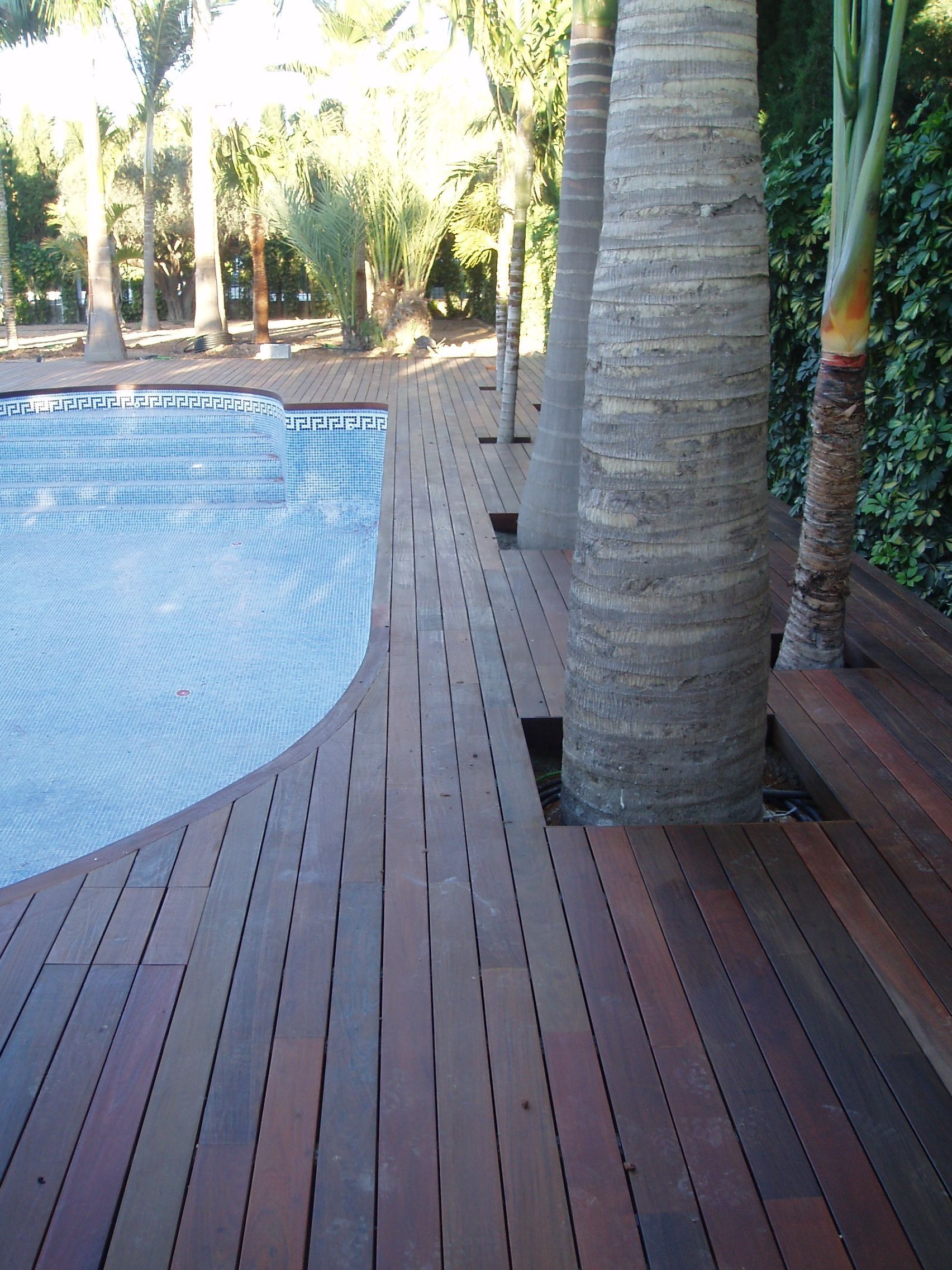 Una terraza de madera con una piscina al fondo.