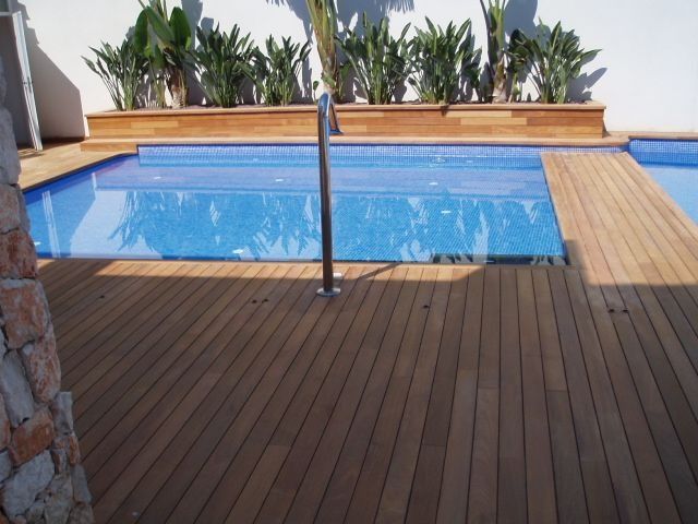 Una terraza de madera con una piscina al fondo.