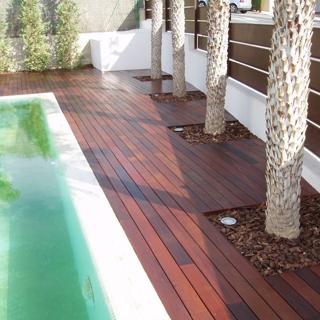 Una piscina con terraza de madera rodeada de árboles.