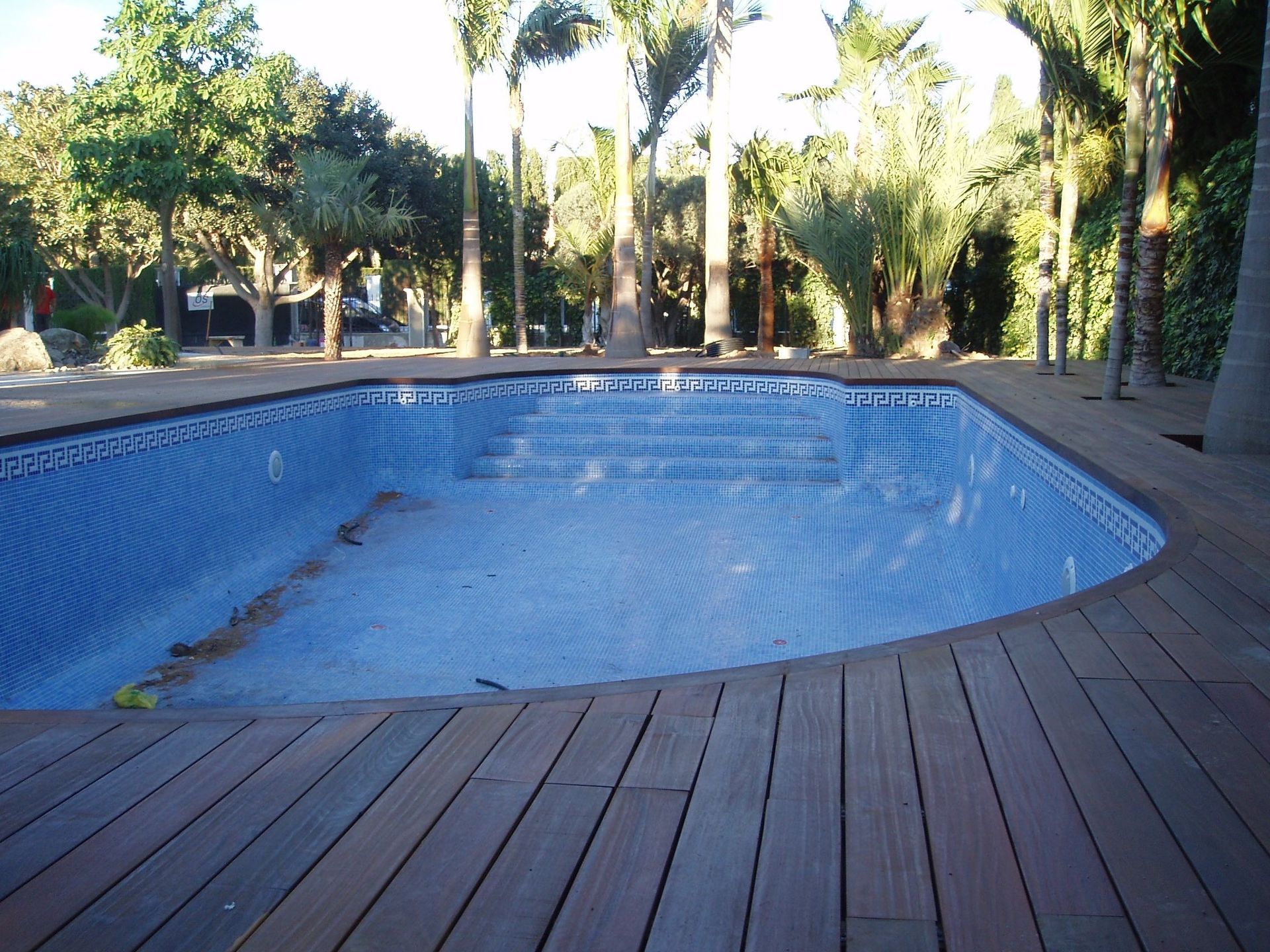 Una piscina vacía rodeada de palmeras y una terraza de madera.
