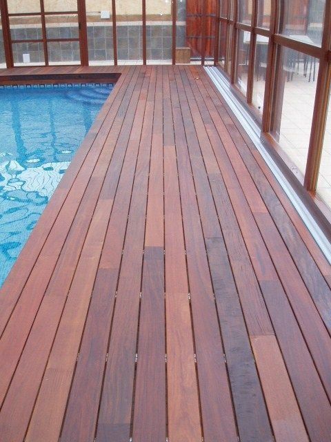 Una terraza de madera con una piscina al fondo.