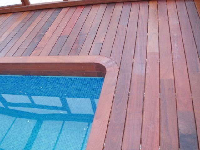 Una terraza de madera con una piscina al fondo.