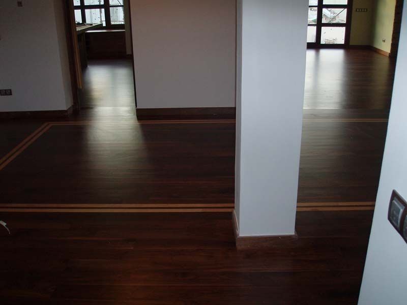 Una habitación vacía con suelo de madera y una columna blanca.