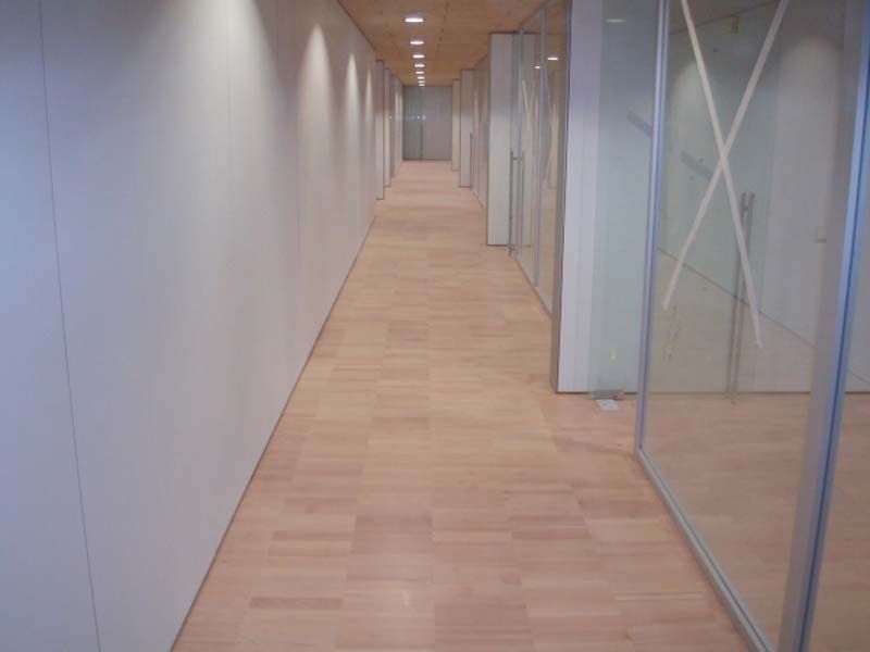 Un largo pasillo con suelo de madera y paredes de cristal.