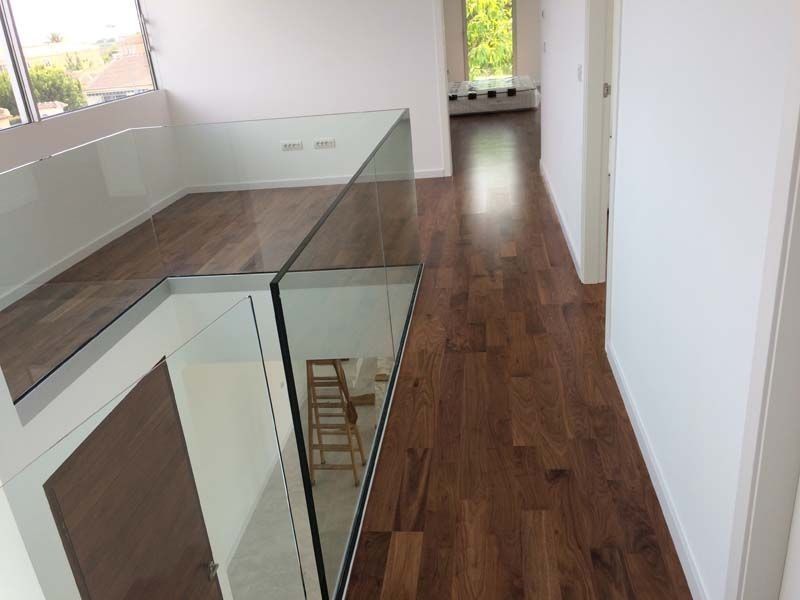 Un pasillo con pisos de madera y barandilla de vidrio.