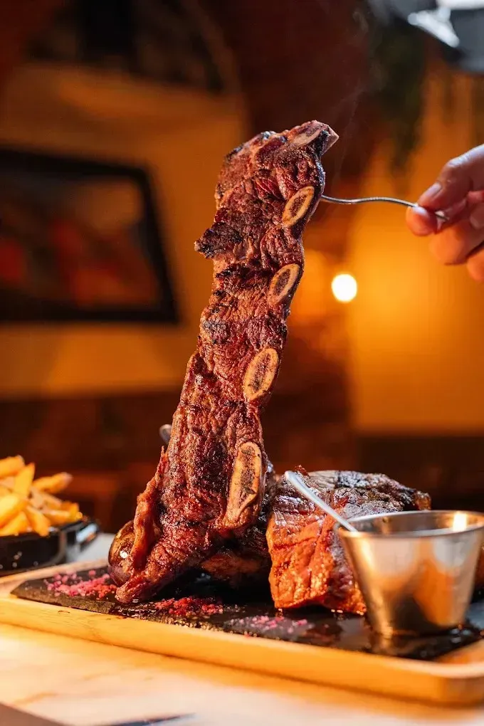 Un gran filete a la parrilla sujeto con un tenedor en un plato, con patatas fritas y salsa en un ambiente
