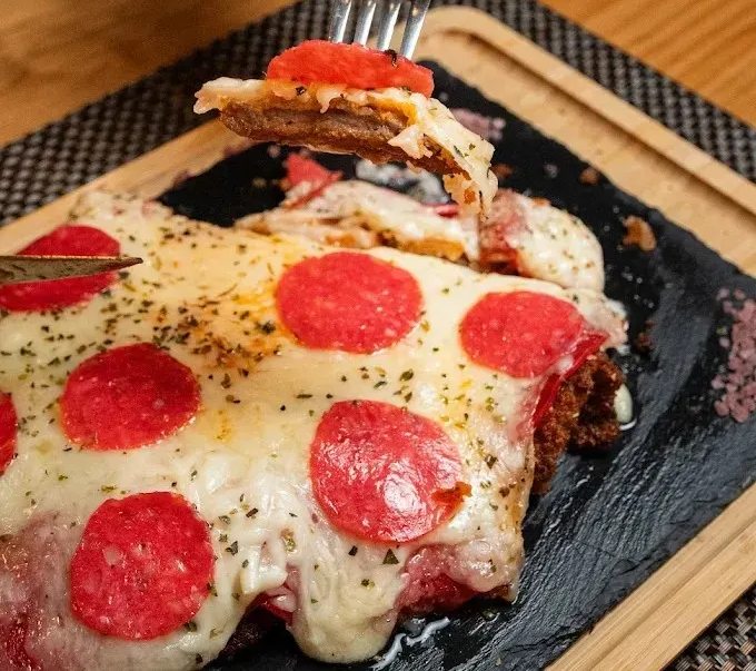 Rebanadas de pizza de pepperoni con queso sobre una tabla de pizarra negra con una bandeja de madera.