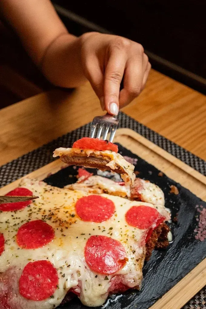 Una mano sostiene un tenedor sobre una pizza de pepperoni con queso en un plato negro.