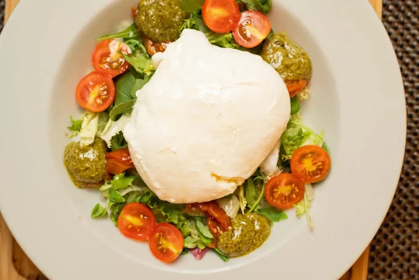 Ensalada Caprese con burrata, tomates cherry, albahaca y verduras en un plato blanco.