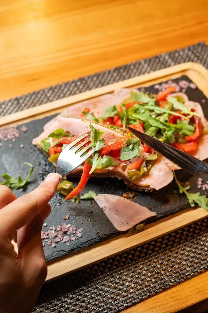 Cortando a mano una colorida ensalada de pescado ahumado en un plato de piedra negra sobre una mesa de madera.