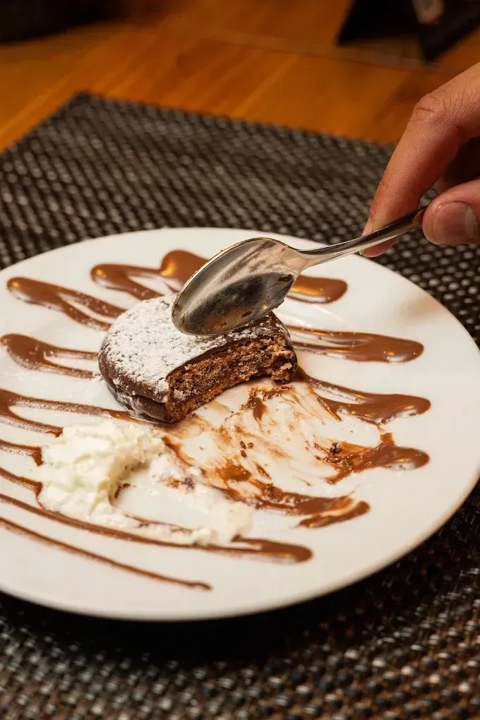 Plato de postre con sirope de chocolate y una cuchara que levanta una porción de pastel espolvoreada con azúcar glas.
