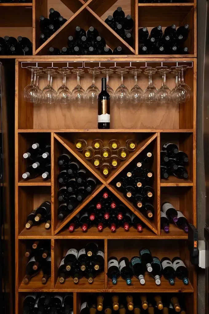Botellero de madera lleno de botellas y copas de vino colgantes