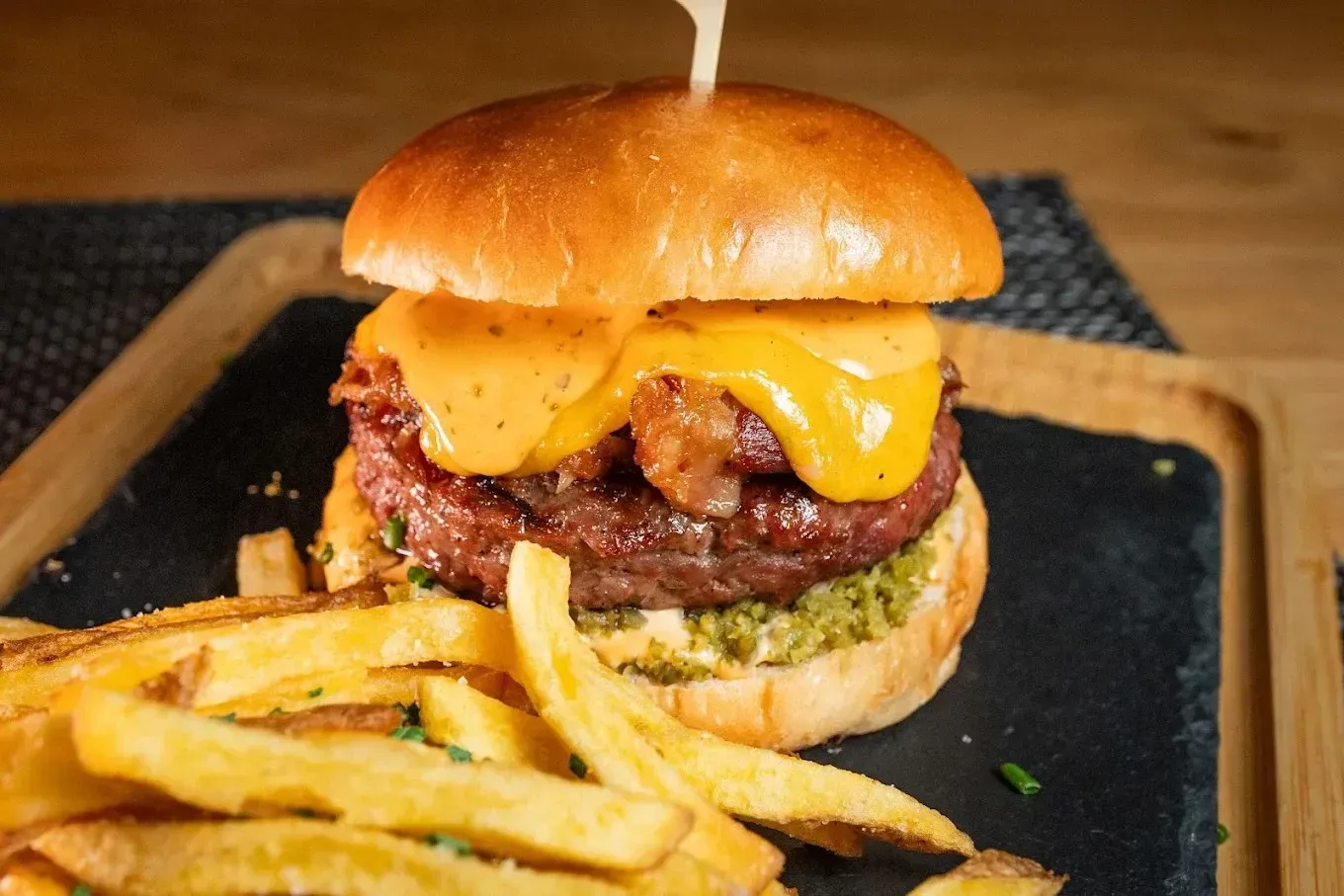 Hamburguesa con queso cheddar derretido y papas fritas en una bandeja de madera.