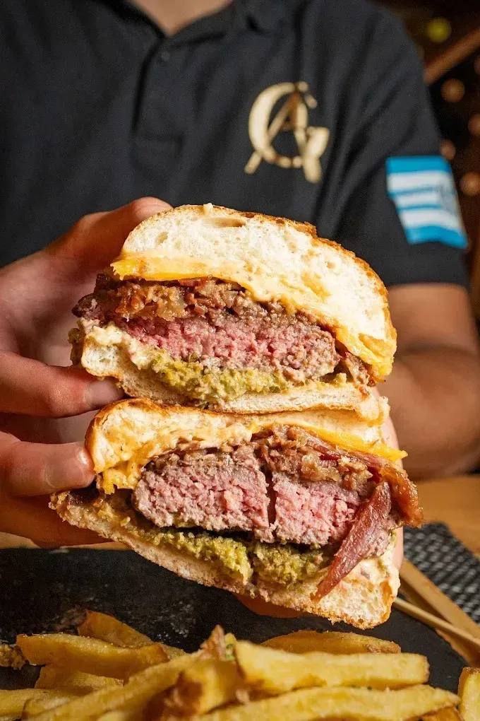 Persona sosteniendo una hamburguesa con queso y papas fritas en un restaurante informal.