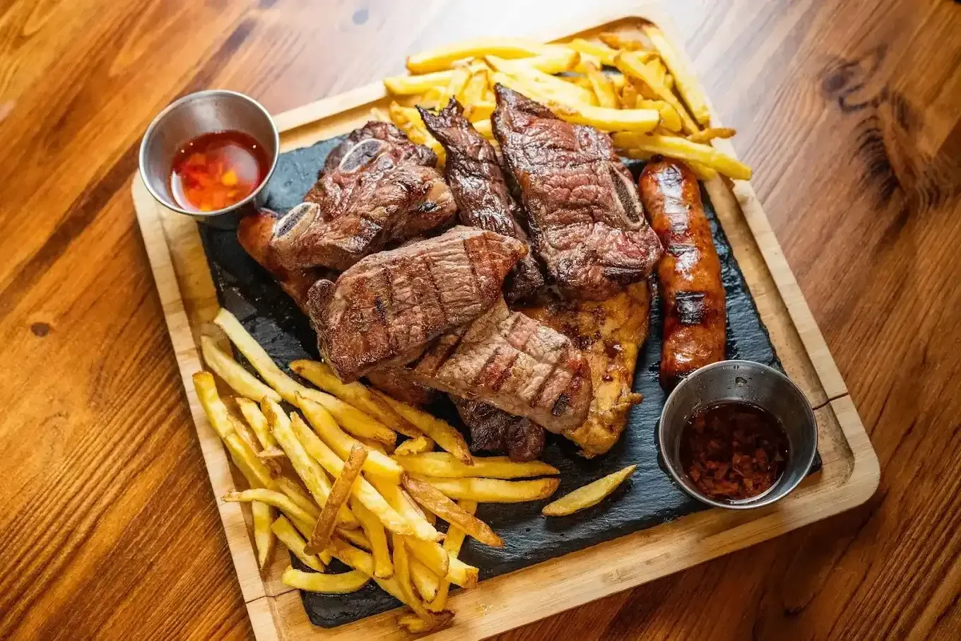 Trocitos de bistec a la parrilla con papas fritas y salsas para mojar en una tabla de madera, vista superior