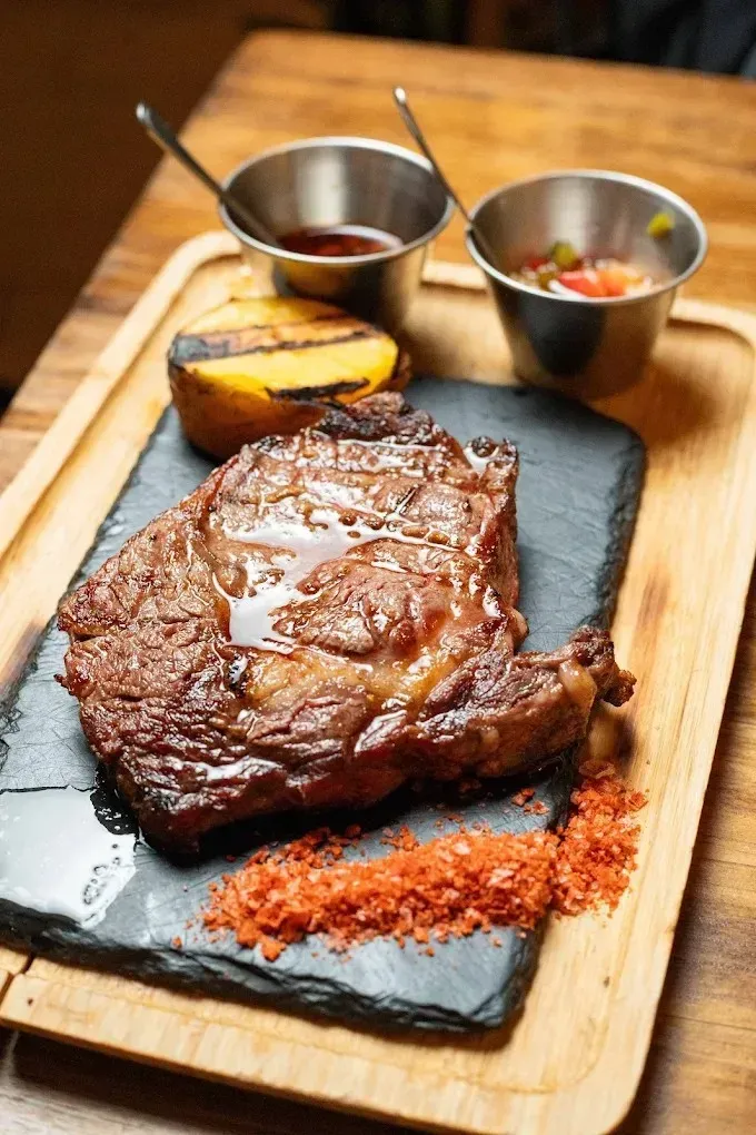 Filete a la parrilla en un plato de pizarra con salsa, limón a la parrilla y dos pequeños 