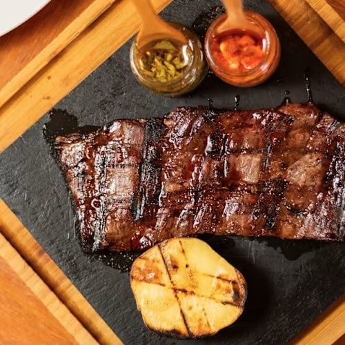 Costillas a la parrilla con dos salsas para mojar y una patata asada sobre una tabla de pizarra negra.