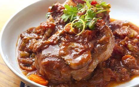 Un plato blanco cubierto con carne y salsa sobre una mesa de madera.
