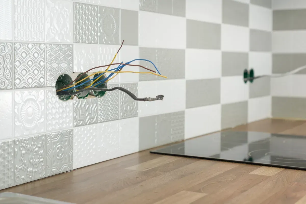Cableado eléctrico en progreso, tomacorriente abierto con cables expuestos contra salpicadura de azulejos