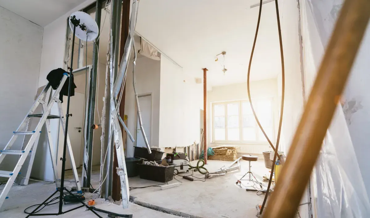 Habitación en construcción, con vigas a la vista, drywall y equipos dispersos.