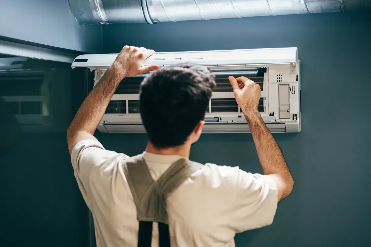 Una persona que instala o repara una unidad de aire acondicionado en una pared.