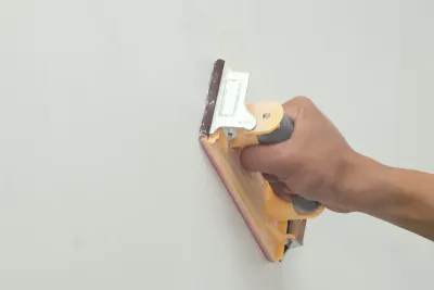 Lijado a mano de una pared blanca con un bloque de lijado.