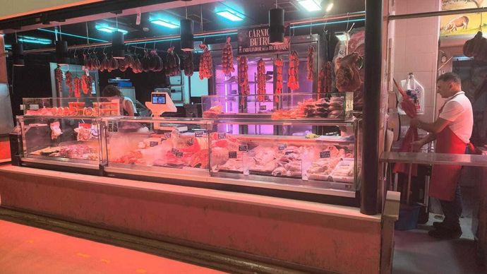 Mostrador de mariscos con iluminación tenue, vitrinas de pescado iluminadas en color rosa y una persona de pie junto al puesto de la derecha.