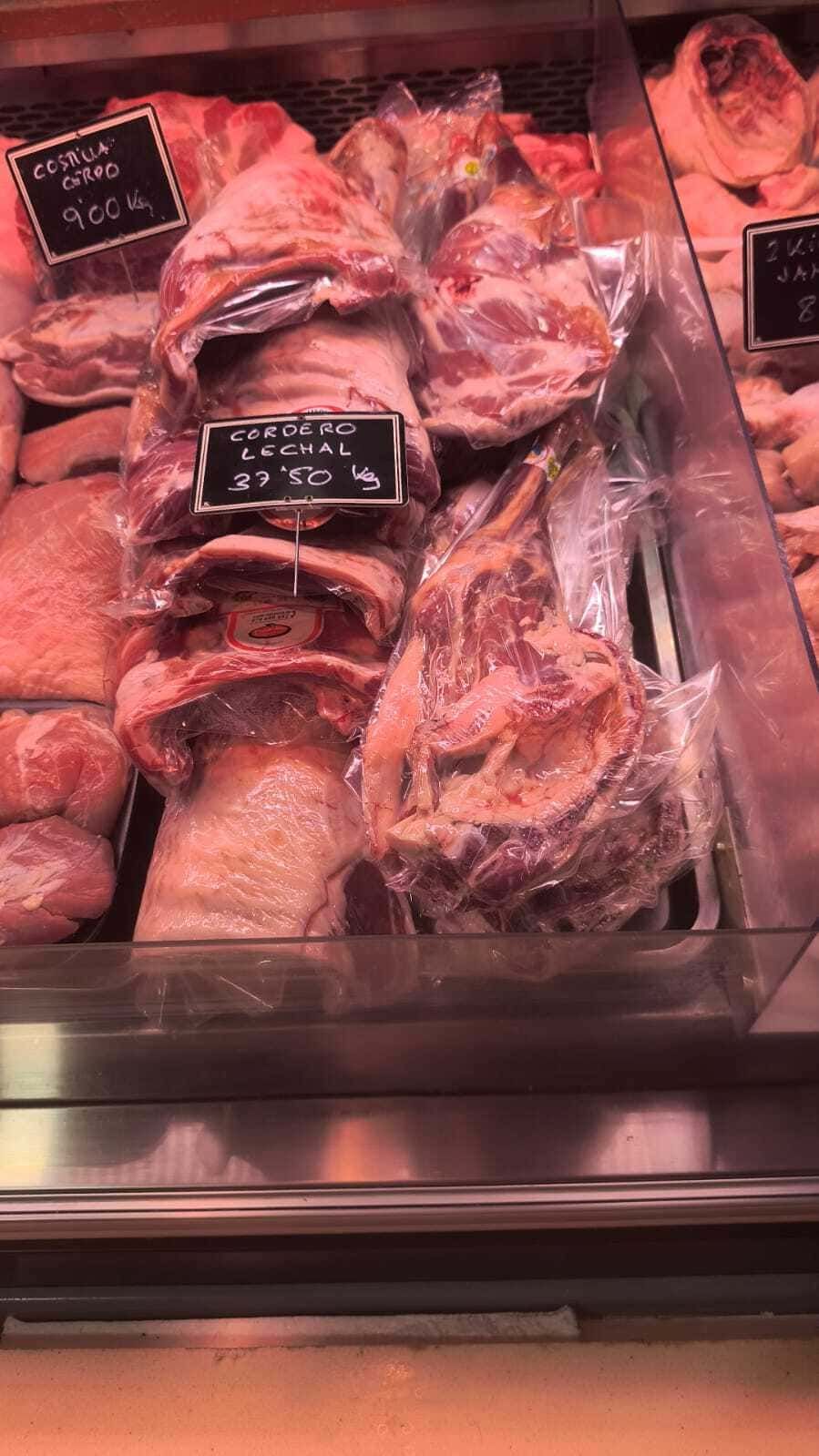 Vitrina con surtido de cortes de carne cruda con etiquetas de precio bajo iluminación rosa.