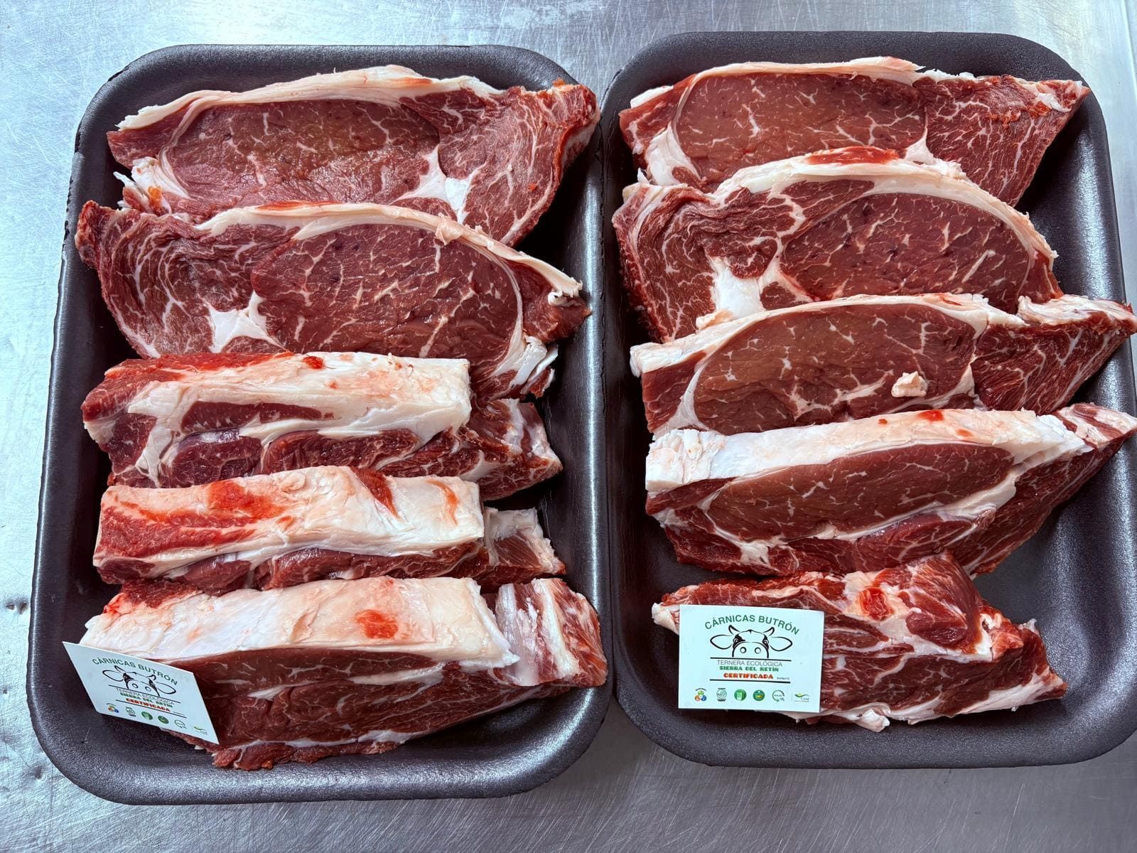 Dos bandejas de cortes de carne de res cruda veteada sobre bandejas de espuma en un expositor de supermercado.
