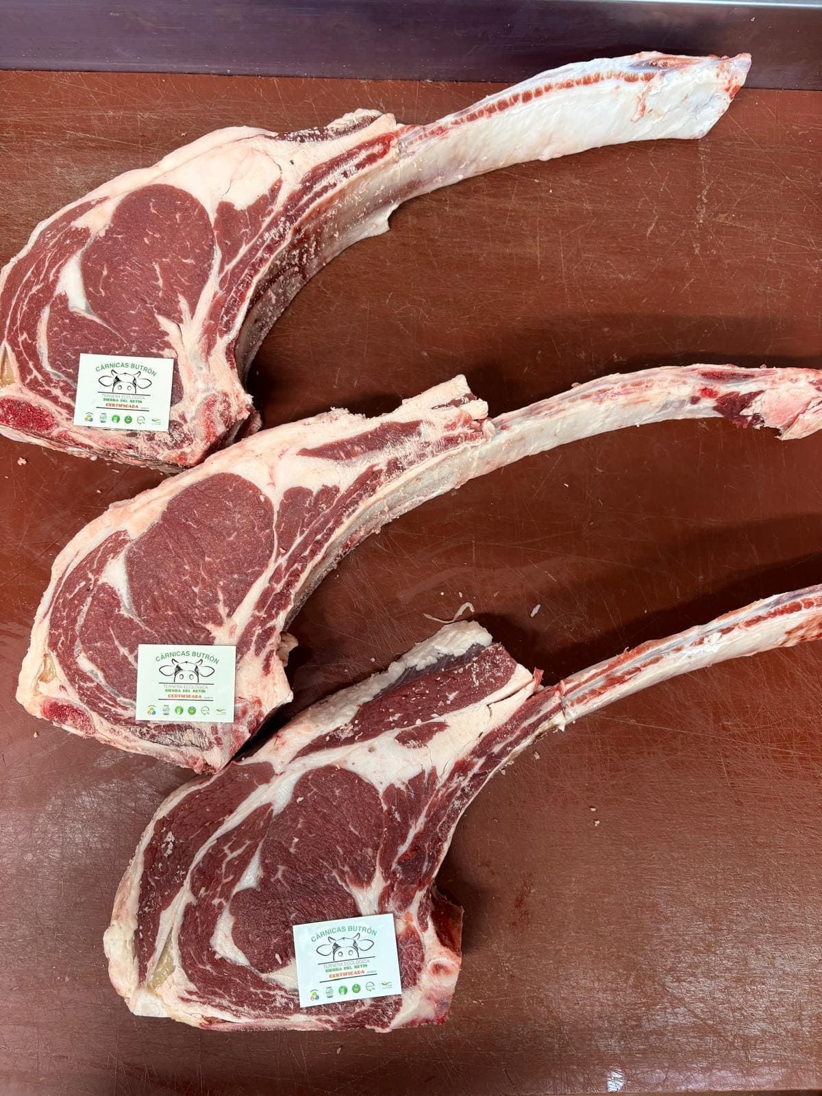 Tres filetes de chuletón tomahawk crudos con hueso largo sobre una tabla de cortar de madera.