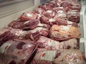 Filas de carne cruda envasada, probablemente de res, en una vitrina refrigerada. La carne está envuelta en plástico transparente con etiquetas.