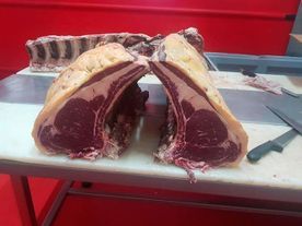 Dos grandes cortes de carne cruda, con carne roja y grasa, sobre una superficie blanca con alrededores rojos.