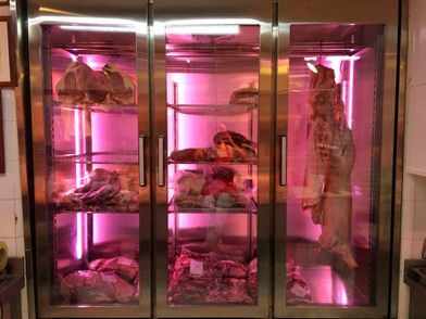 Vitrina de carne iluminada con luz rosa, que muestra diversos cortes de carne en una carnicería.