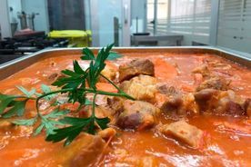 Carne guisada en salsa roja, adornada con perejil, en una bandeja de acero inoxidable, probablemente en una cocina comercial.