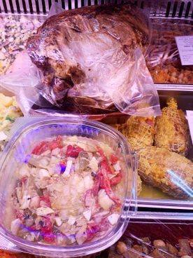 Vitrina con productos alimenticios preparados: carne asada envuelta en film, ensalada en recipiente transparente y hamburguesas de carne envueltas.