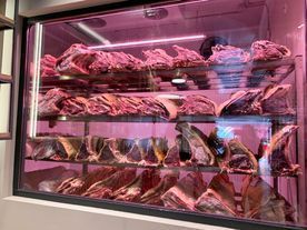 Vitrina con filas de grandes cortes de carne roja cruda, iluminada por luz rosa.