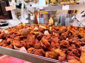 Una bandeja rebosante de trozos de carne fritos y dorados. El ambiente parece el de una carnicería o un puesto de charcutería.