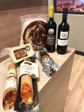 Tabla de embutidos con botellas de vino tinto, quesos y embutidos expuestos sobre una superficie de madera.