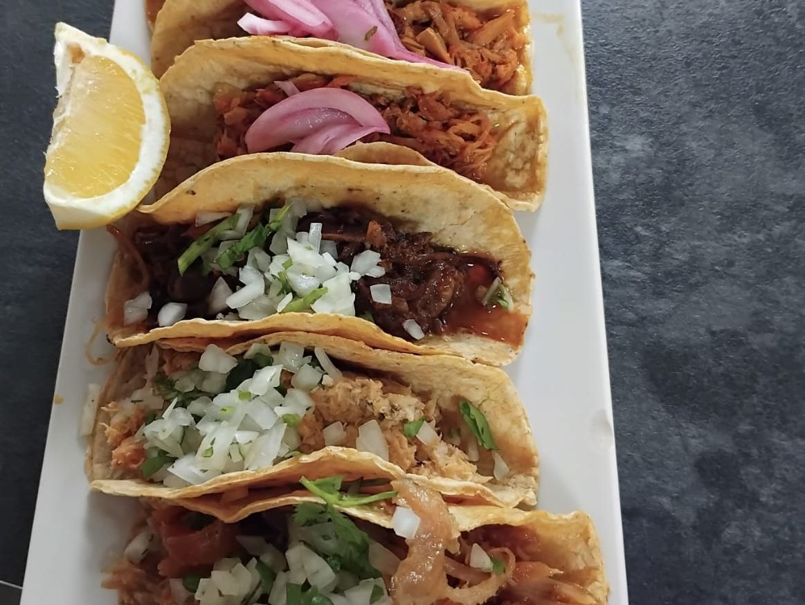 Un plato blanco cubierto con una variedad de tacos y una rodaja de limón.