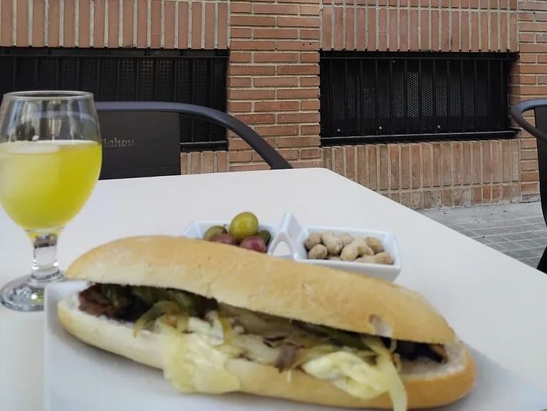 Un sándwich está sobre una mesa junto a un vaso de jugo de naranja.