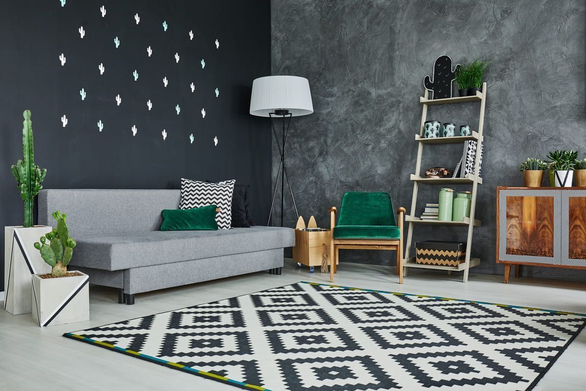Sala de estar moderna con sofá gris, pared decorativa negra, alfombra estampada, silla verde y lámpara de pie.