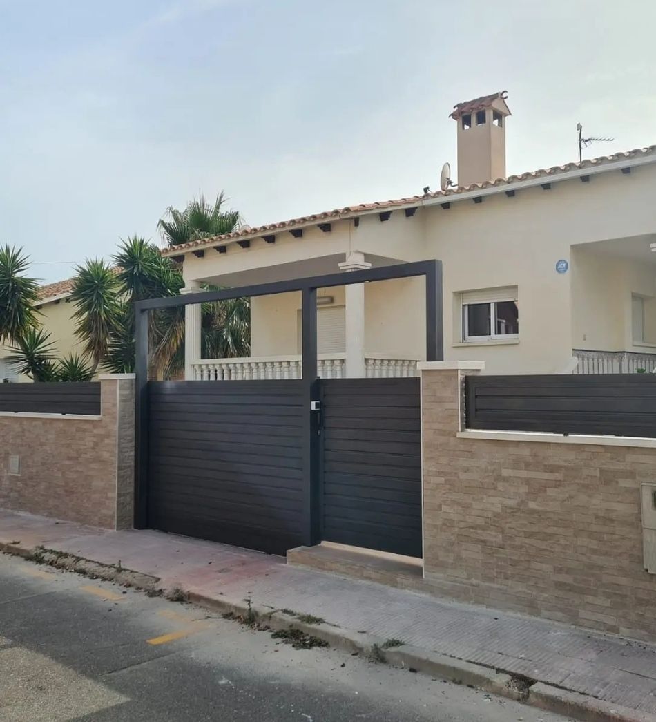 Exterior de una casa moderna con una puerta negra, paredes beige y una acera a lo largo de la calle.