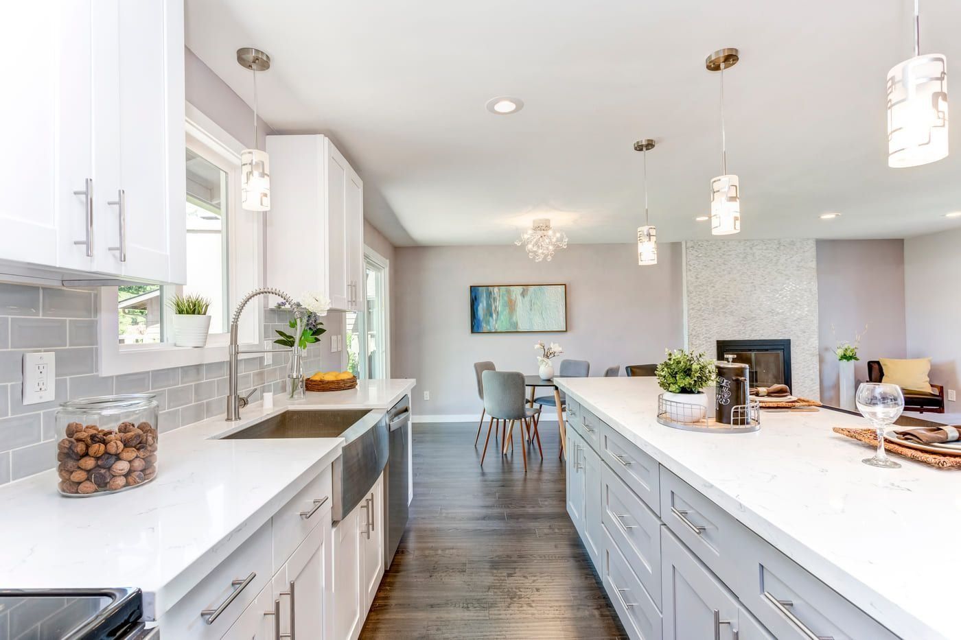 Cocina moderna y luminosa con armarios blancos, encimeras de mármol y un comedor al fondo.
