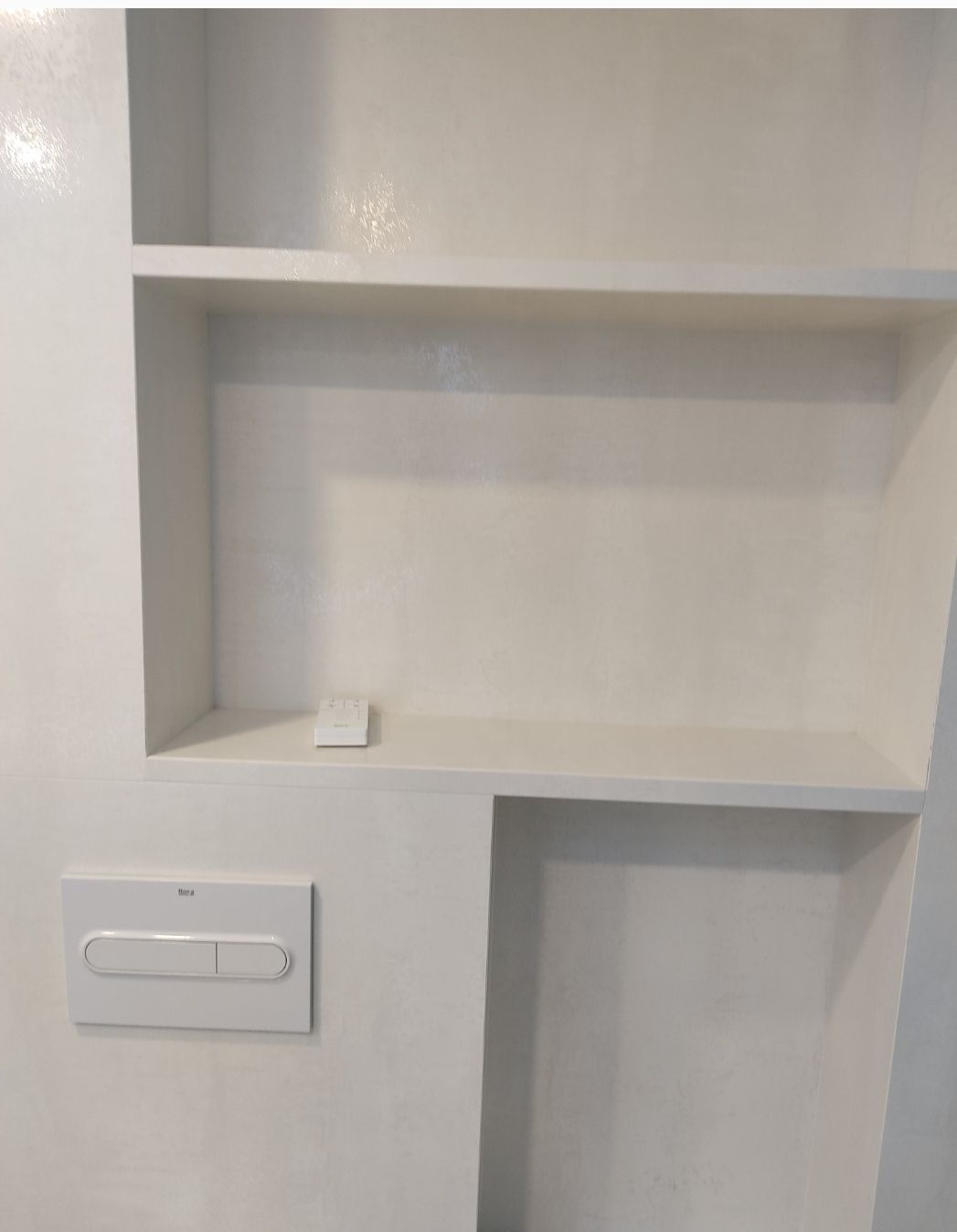 Estanterías blancas empotradas en la pared, con interruptor de luz y un nicho rectangular abierto debajo.