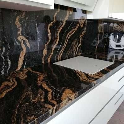 Cocina moderna con encimera y protector contra salpicaduras de mármol negro y dorado, gabinetes blancos y placa de cocción integrada.
