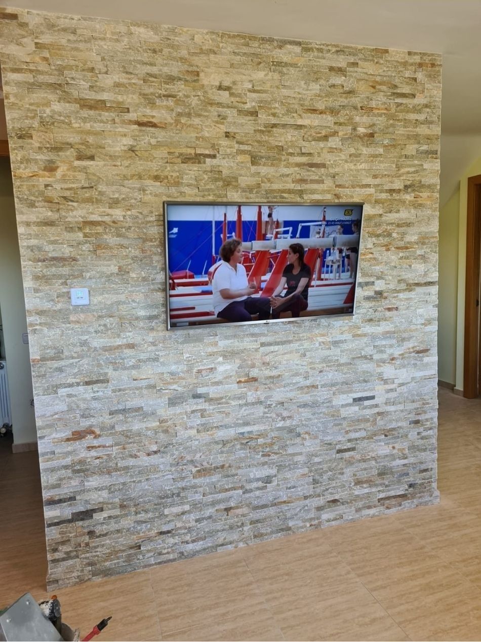 Televisor montado en la pared sobre una pared decorativa revestida de piedra apilada en una habitación con suelo de madera clara.